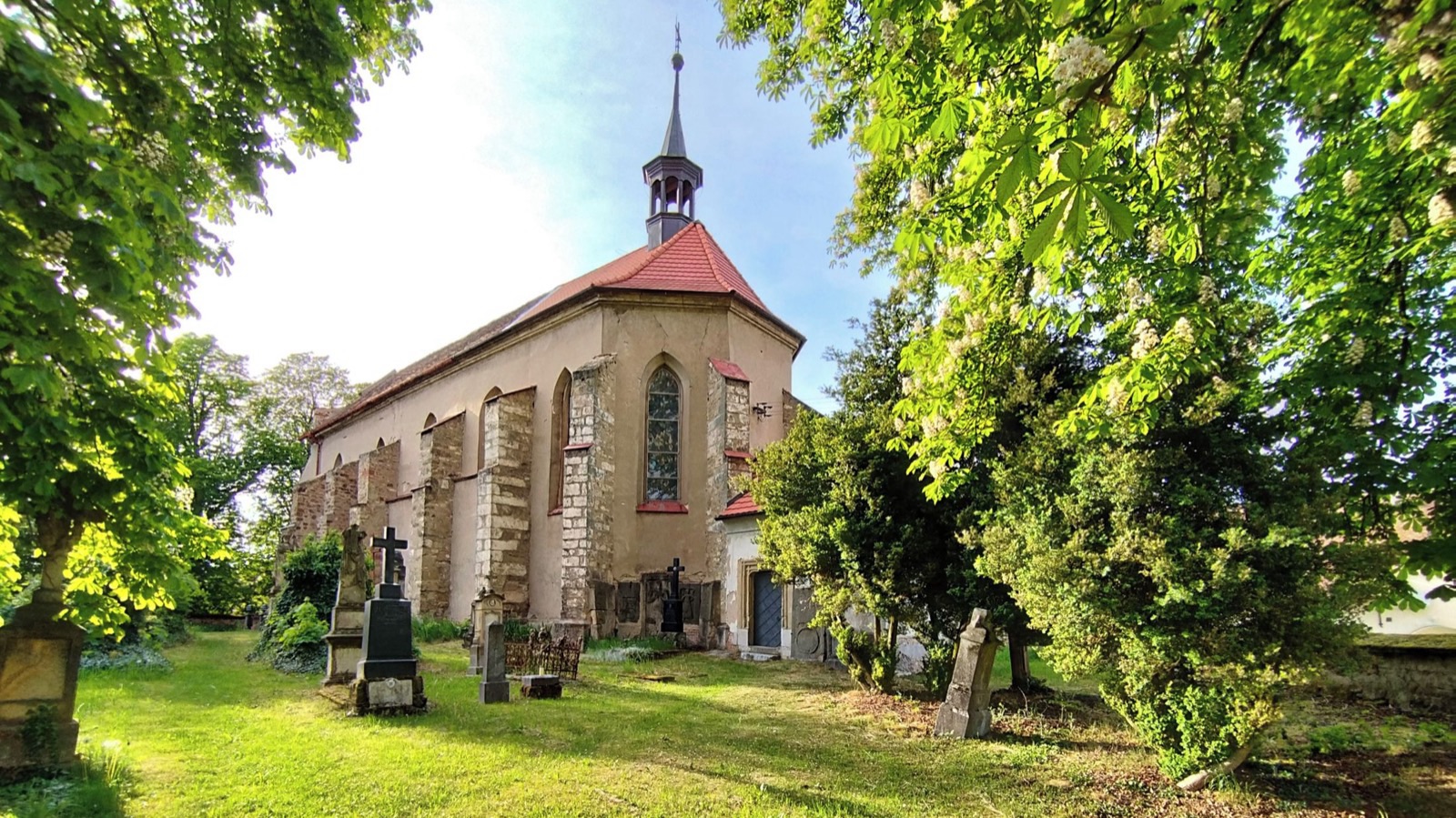 Kostel sv. Václava s červenou střechou a vížkou mezi stromy na hřbitově